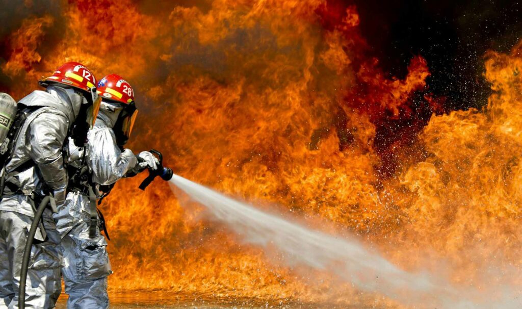 firefighter spraying water hose onto massive fire
